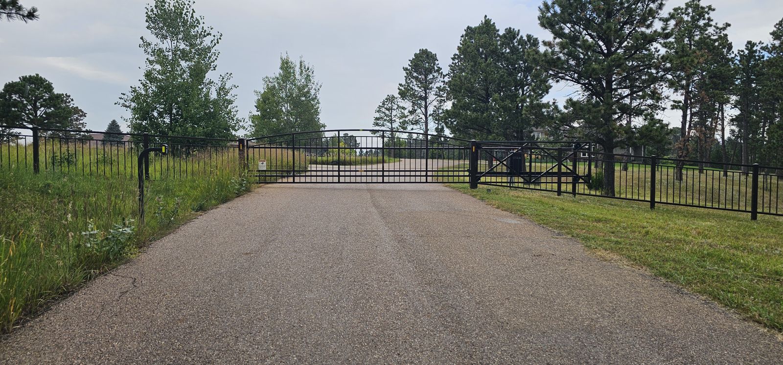 Black ornamental gate and matching fence along a paved drive