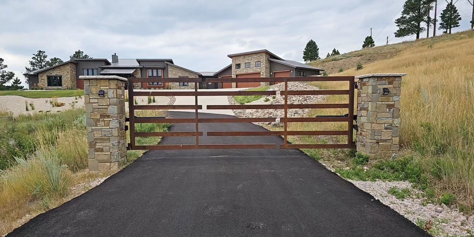Modern corten steel driveway gate with stone masonry pillars